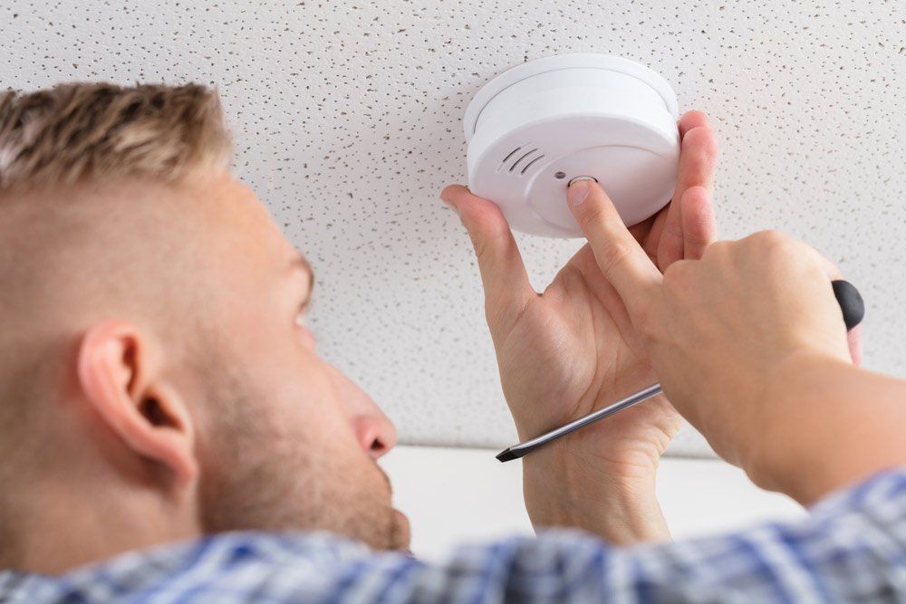 Low Angle View Of A Person's Hand Installing Smoke Detector On Ceiling Wall At Home — Residential Electrical Contractor in Redlynch, QLD