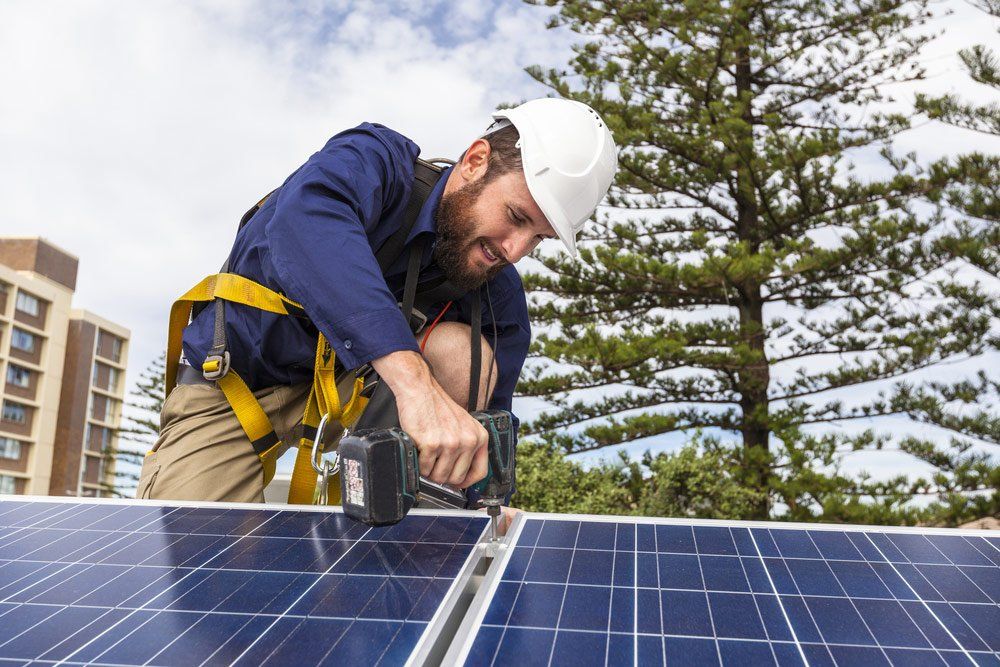 Solar Panel Technician With Drill Installing Solar Panels On Roof — Electrical Services in Cairns, QLD