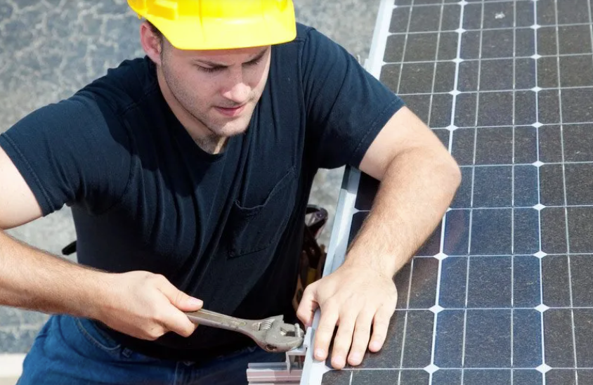 A man wearing a hard hat is working on a solar panel.