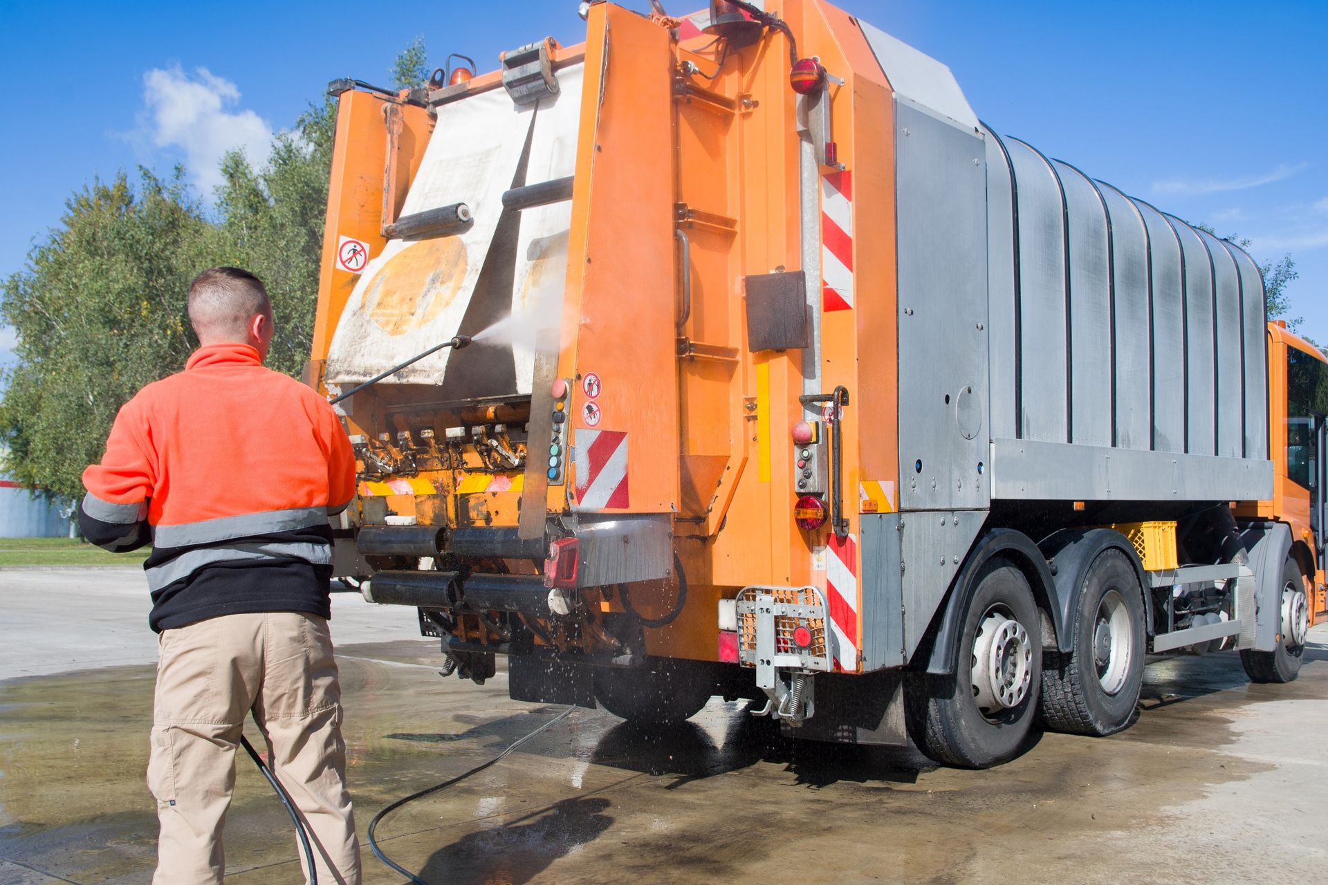 A man is washing a garbage truck with a high pressure washer.