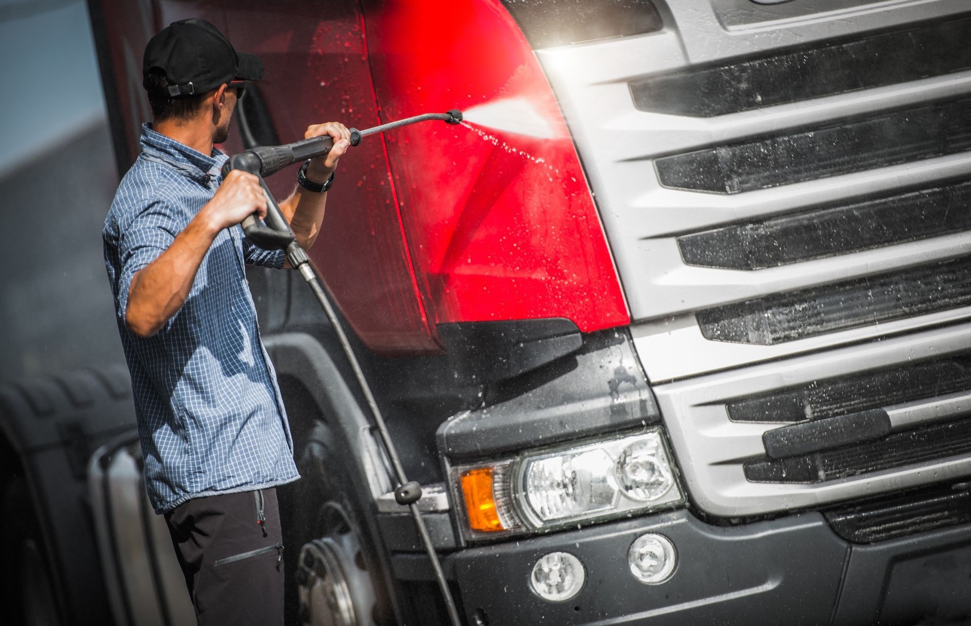 A man is washing a truck with a high pressure washer.