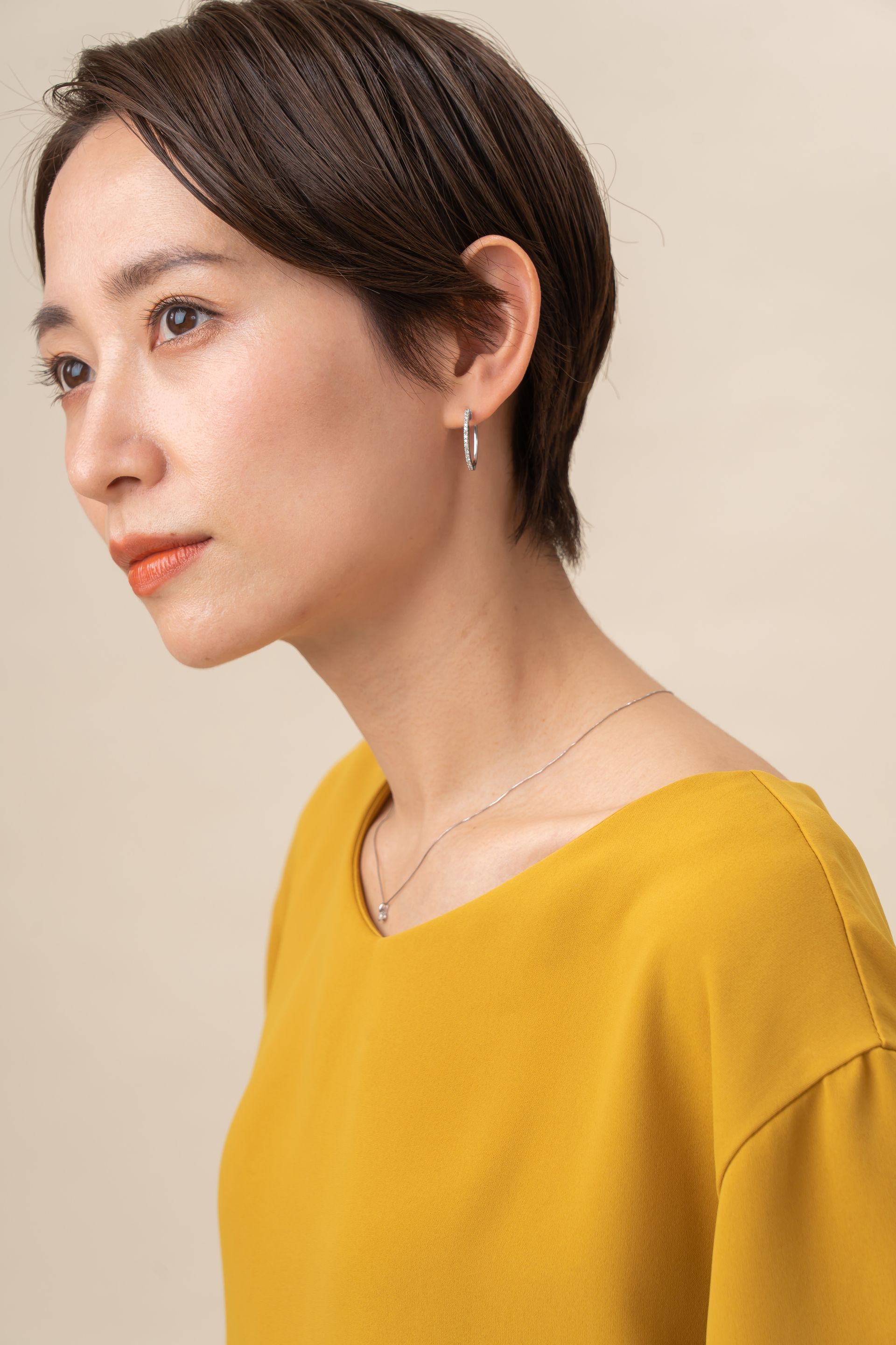 a woman with short hair is wearing a yellow shirt and earrings .