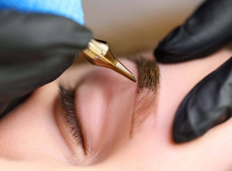 A woman is getting a tattoo on her eyebrows.