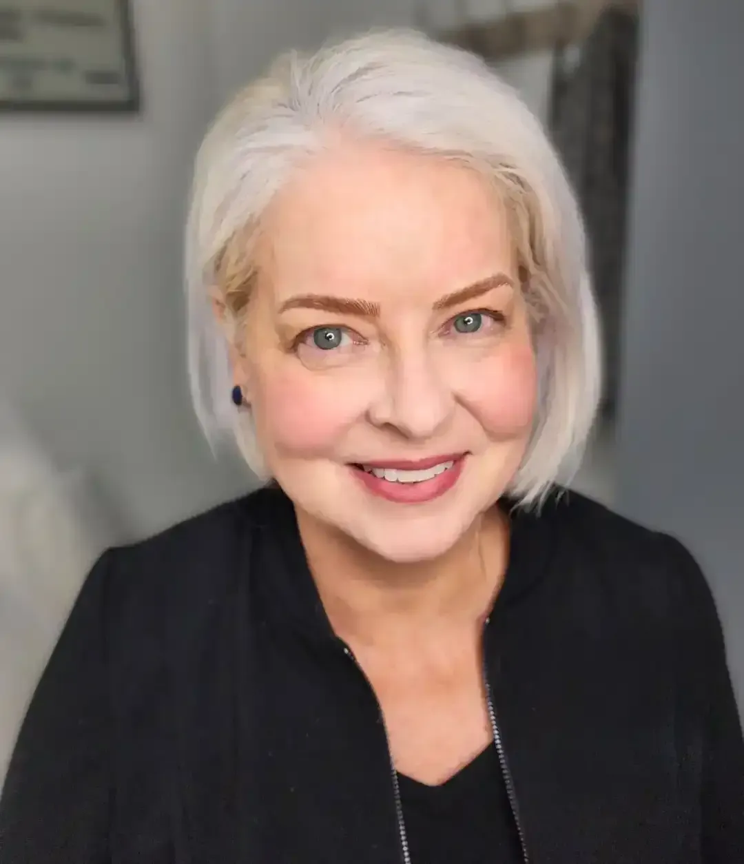 A woman with white hair is wearing a black jacket and smiling for the camera.
