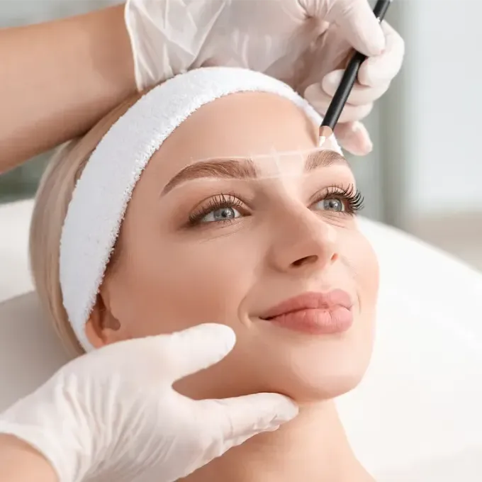 A woman is getting her eyebrows drawn by a professional.