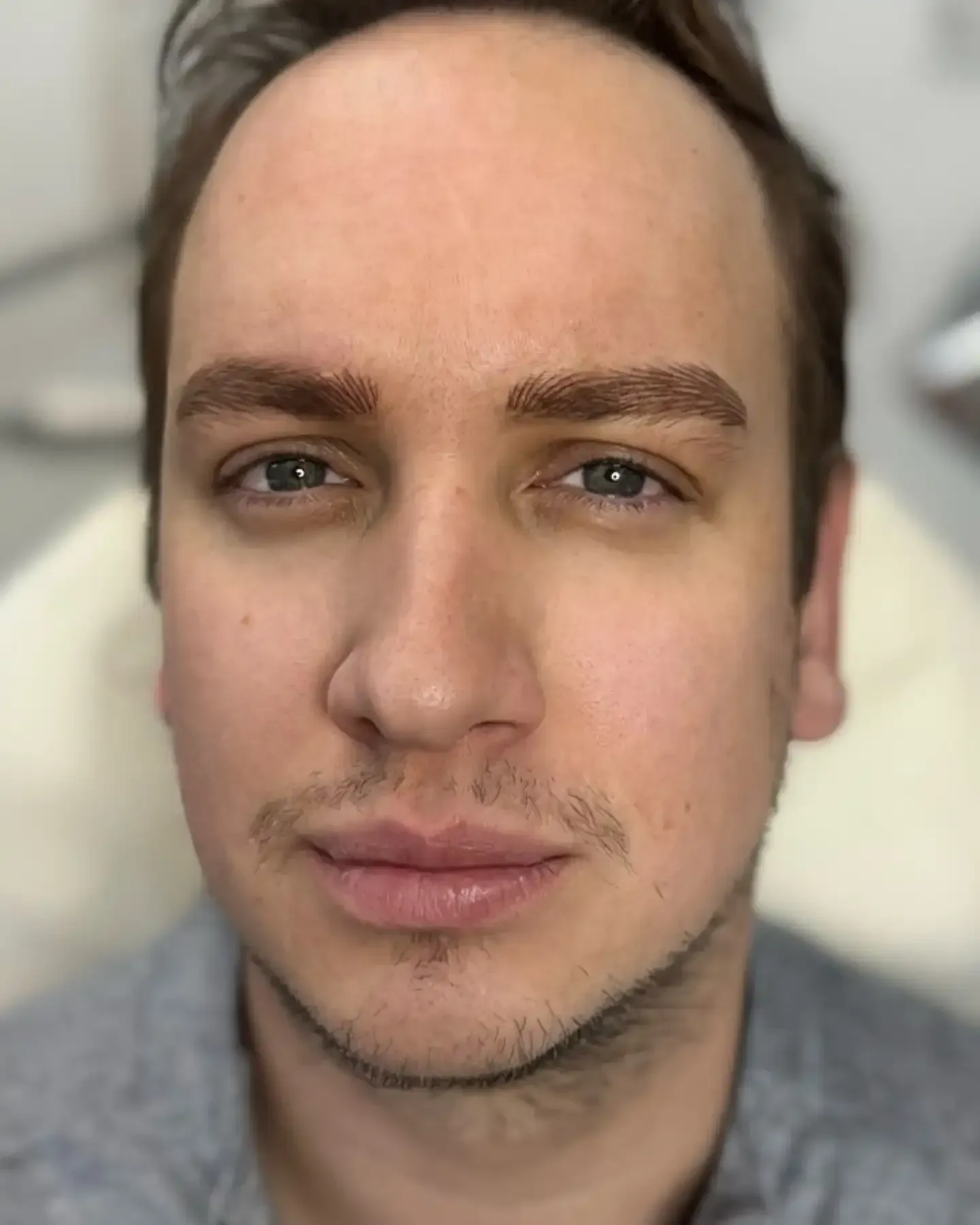 A close up of a man 's face with a beard and a gray shirt.