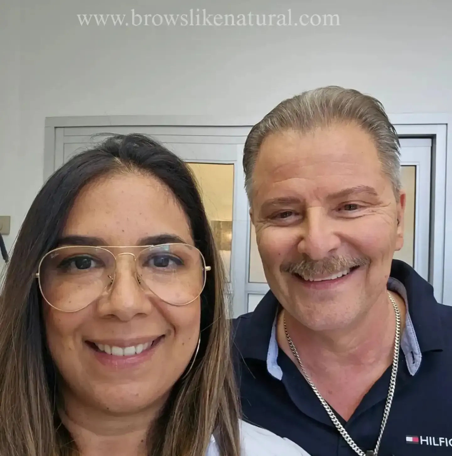 A man and a woman are posing for a picture with the website www.browslikenatural.com in the corner
