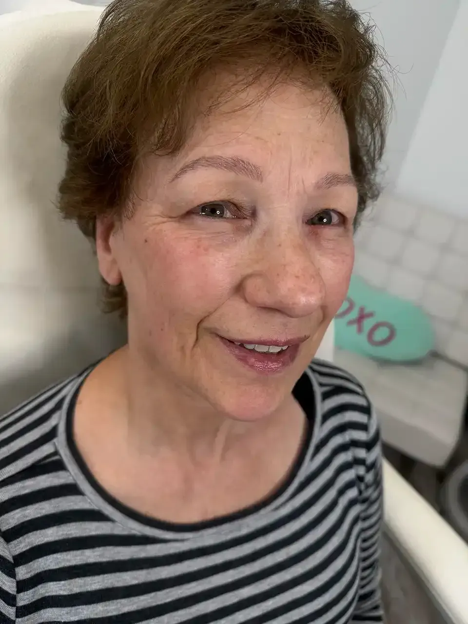 A woman in a striped shirt is smiling while sitting in a chair.