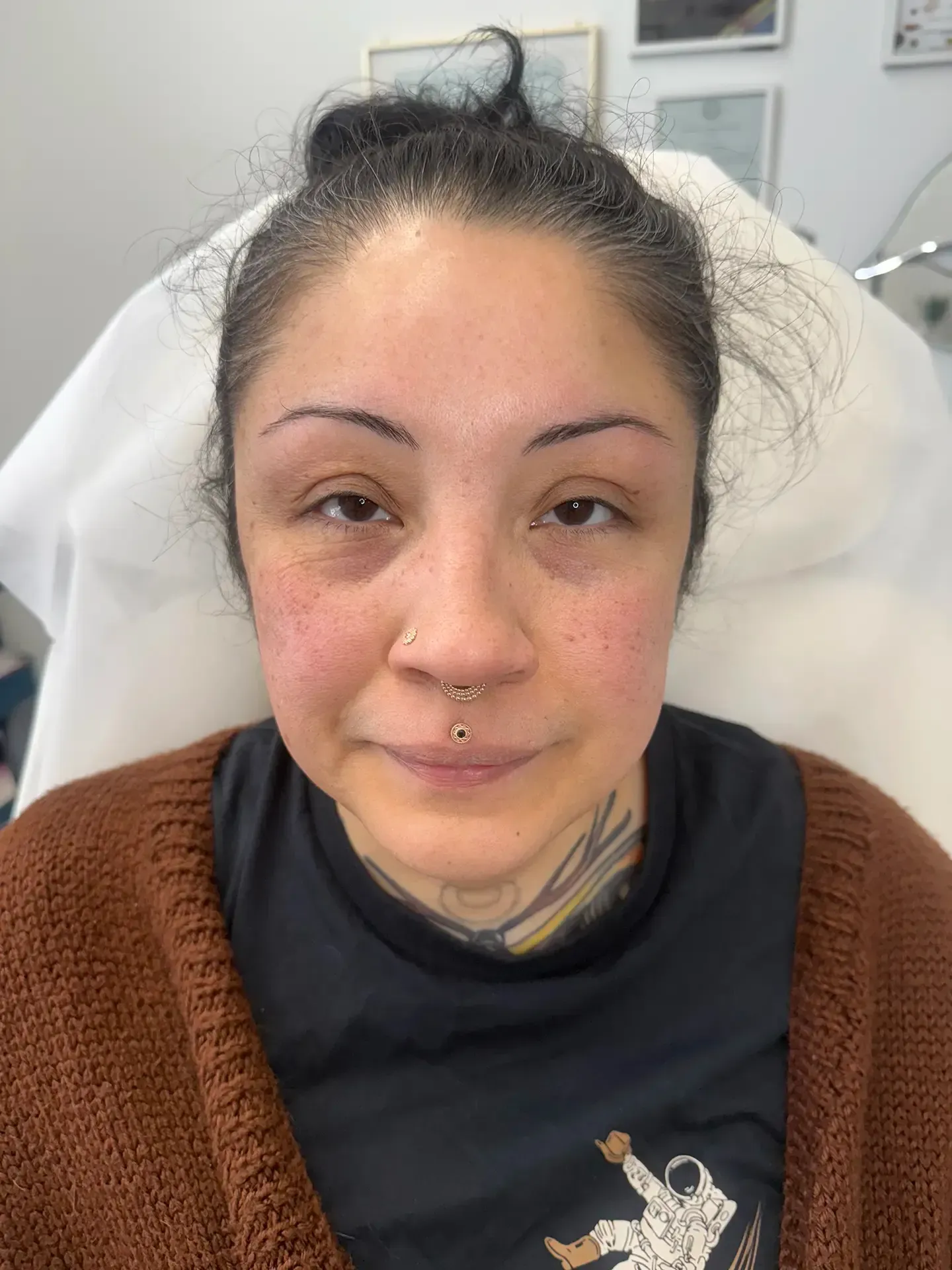 Woman with dark hair in a bun, nose and lip piercings, and wearing a brown sweater