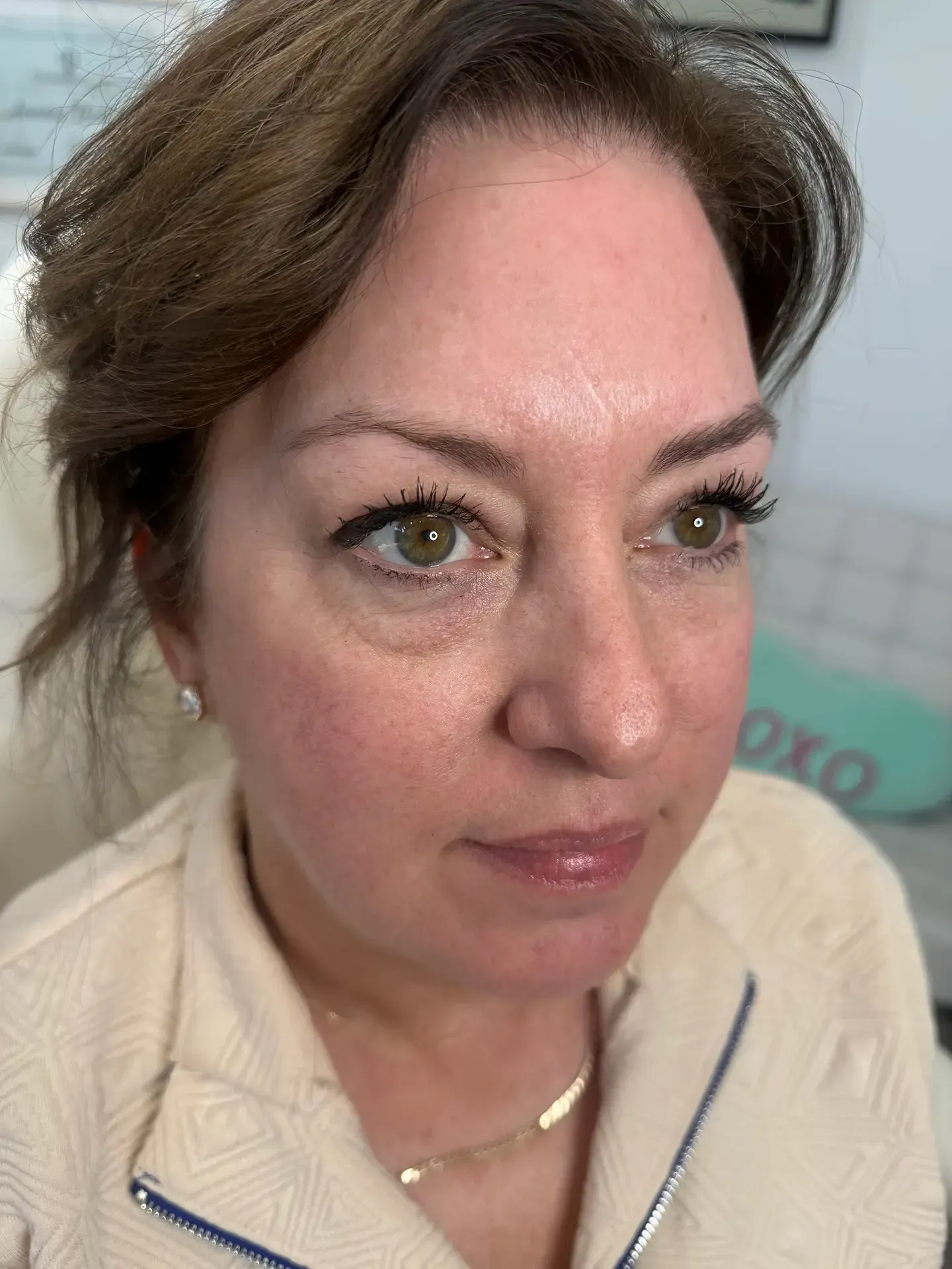 Woman with brown hair looking slightly to the right, wearing light-colored clothing. She has slight bags under her eyes.