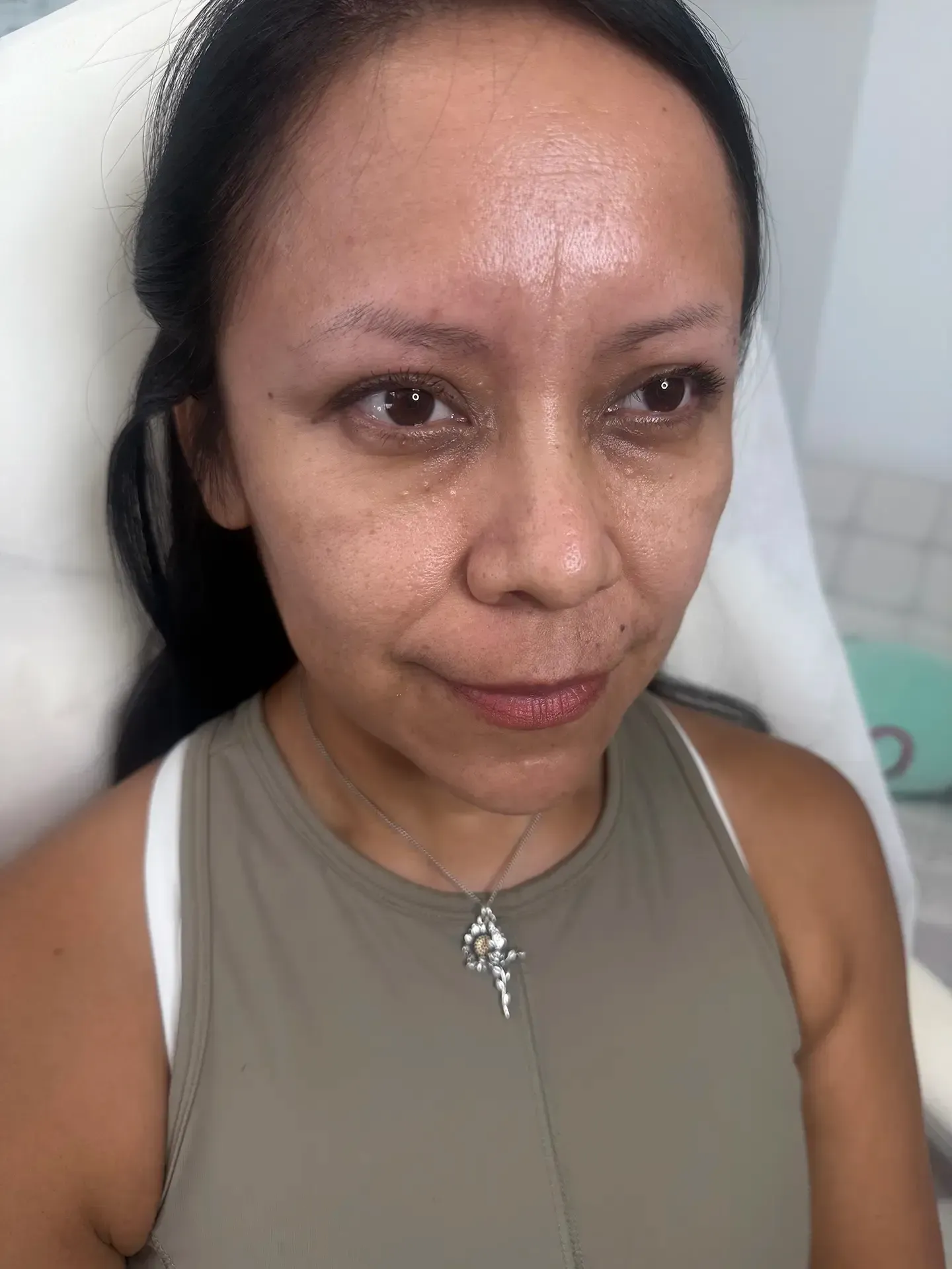 Woman with dark hair, wearing a green top, looking directly at the camera. She is in a seated position indoors.