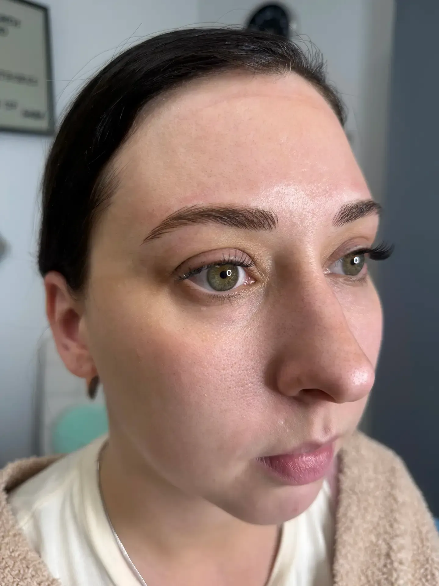 Woman with light skin and green eyes, looking off to the right. She has filled-in eyebrows. Wearing a cream-colored shirt.