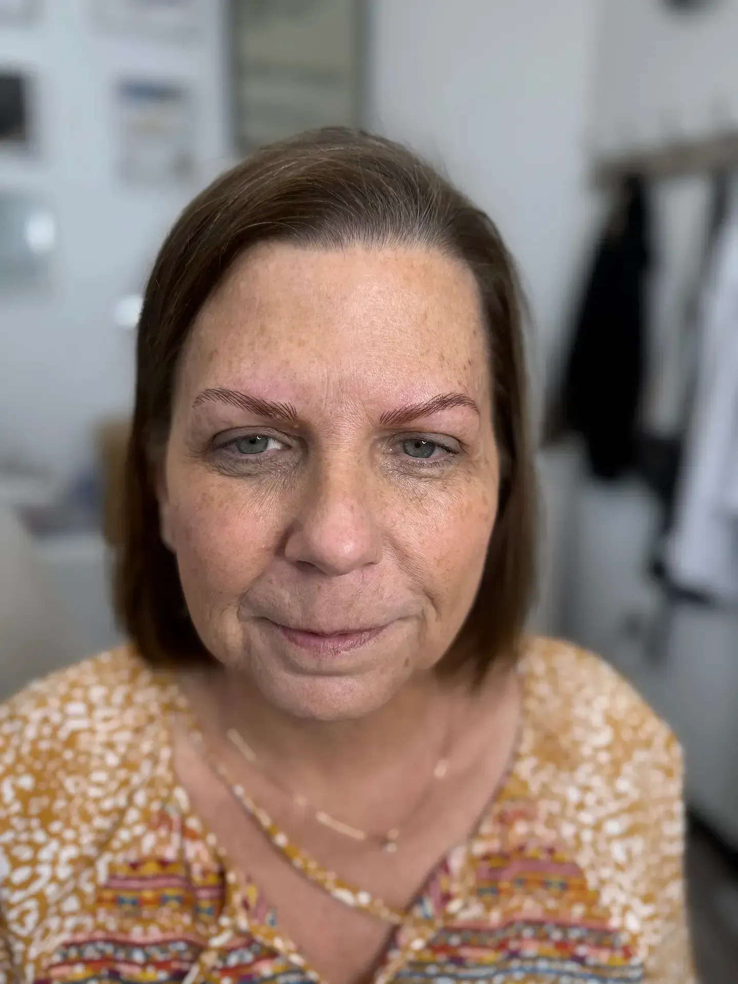 Woman with short brown hair and a yellow floral blouse.