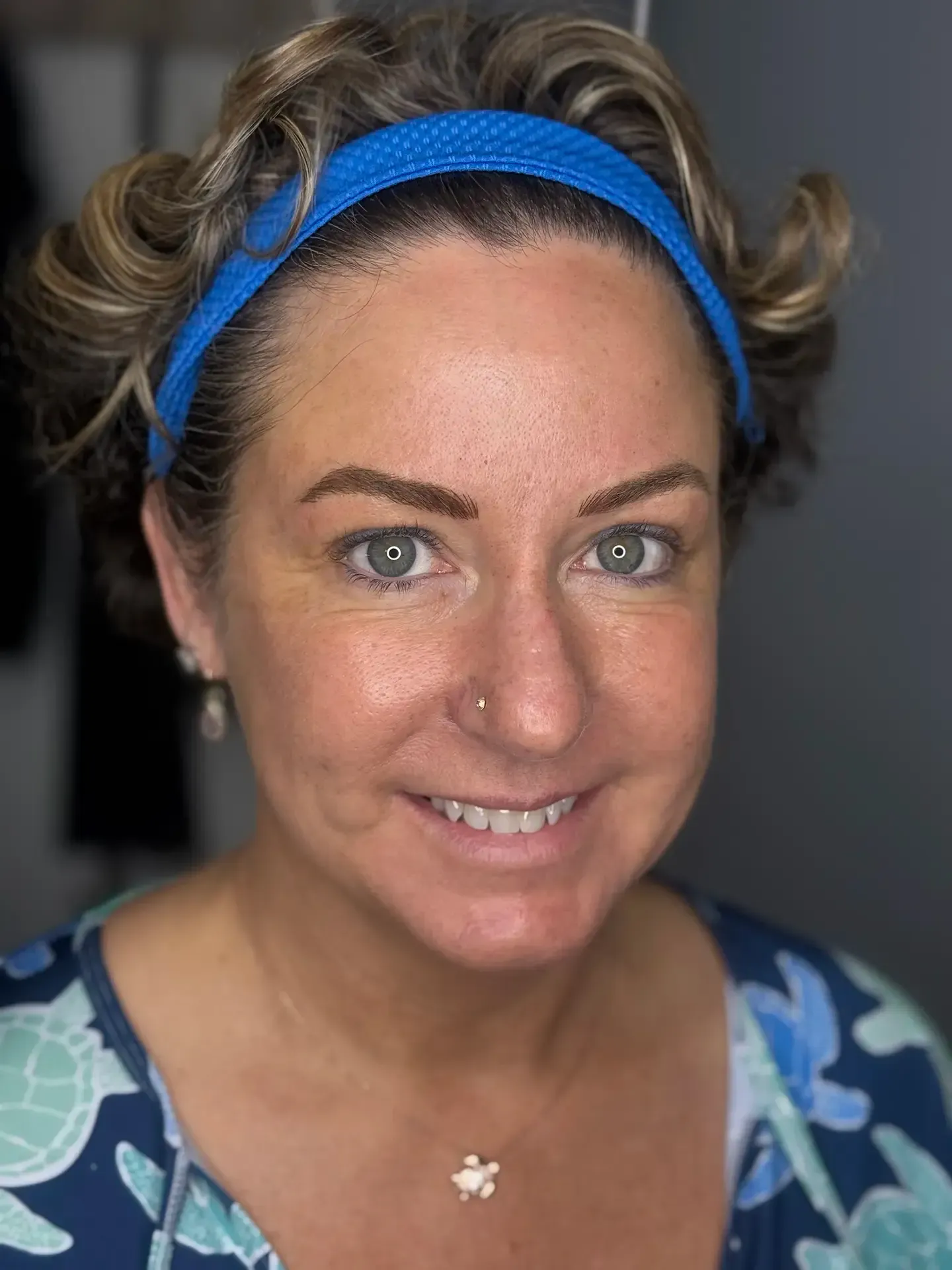 Woman with curly brown hair wearing a blue headband, smiling at the camera.