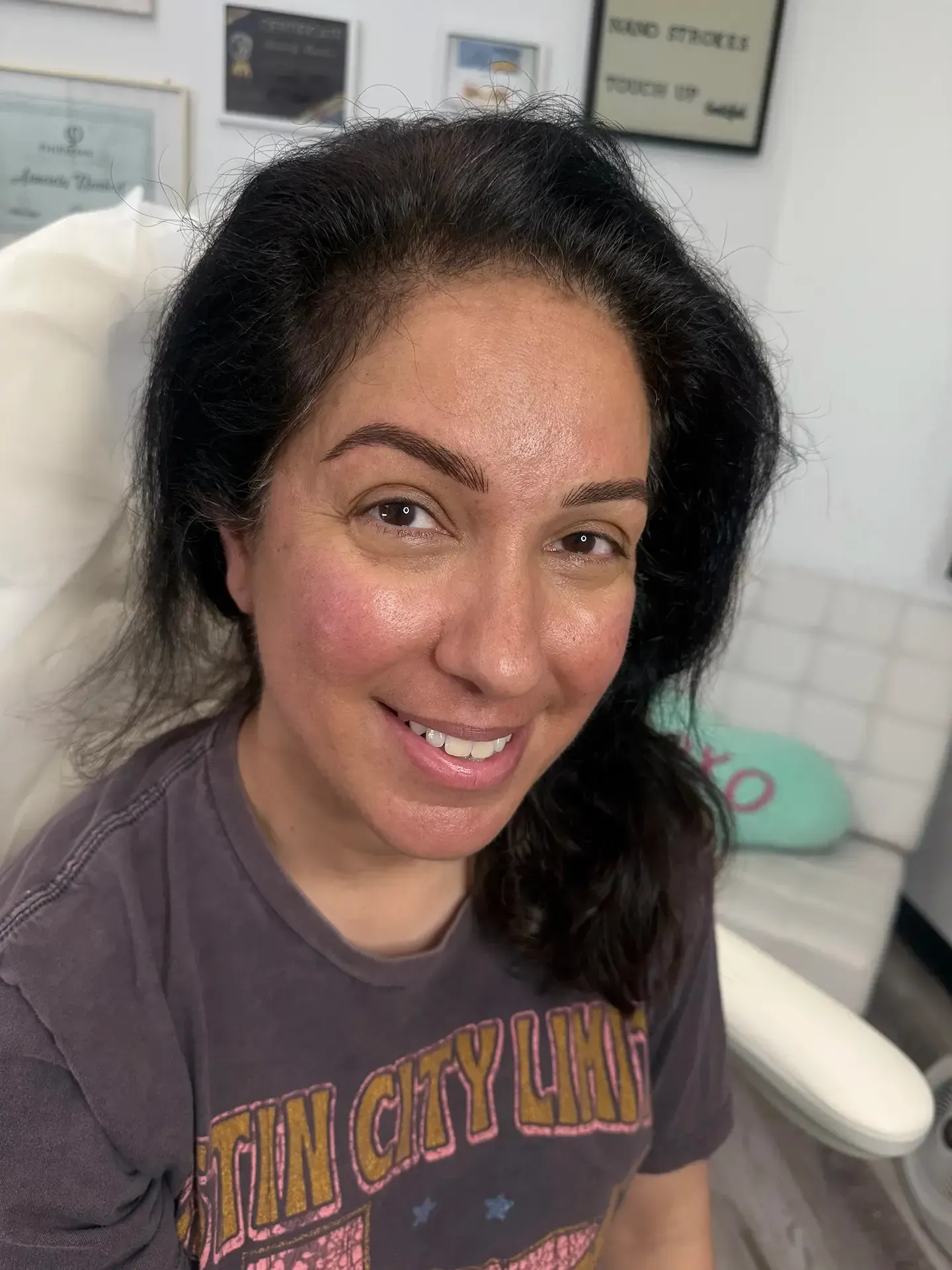 A woman with dark hair and newly-done eyebrows smiles. She's in a clinic, with framed certificates on the wall.