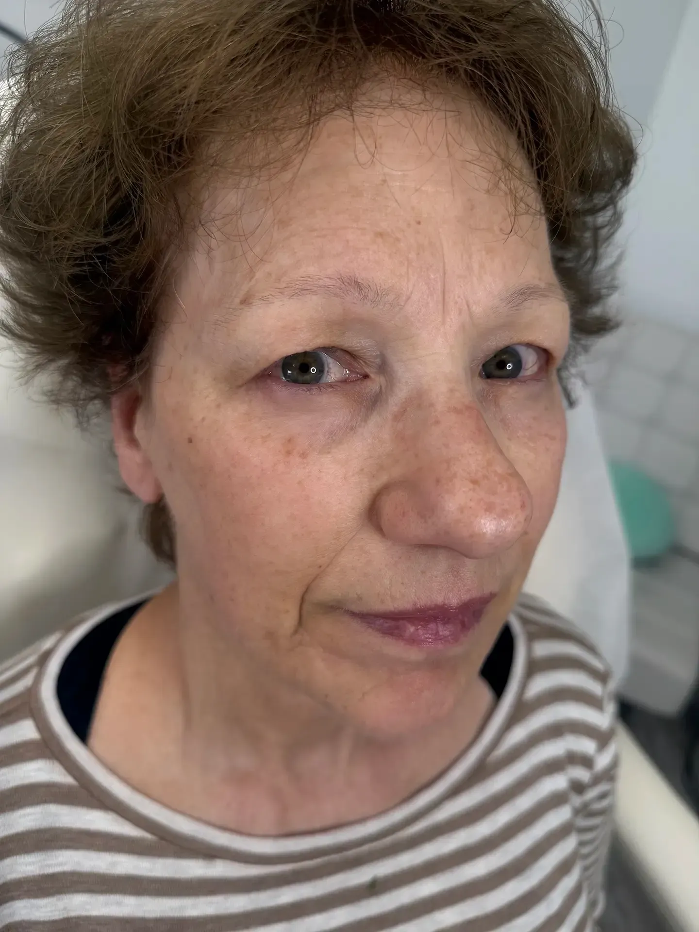 Woman with light skin, brown hair, and a striped shirt. She looks directly at the camera with a neutral expression.
