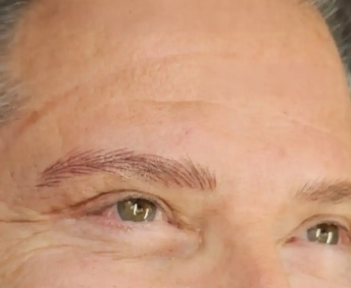 Close-up of a person's face with light brown, well-defined eyebrows. Green eyes and a slight smile.