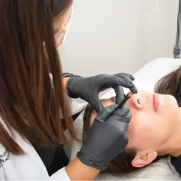 A woman wearing black gloves is examining a woman 's face.