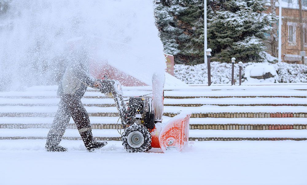 man using a snowblower to clear a path
