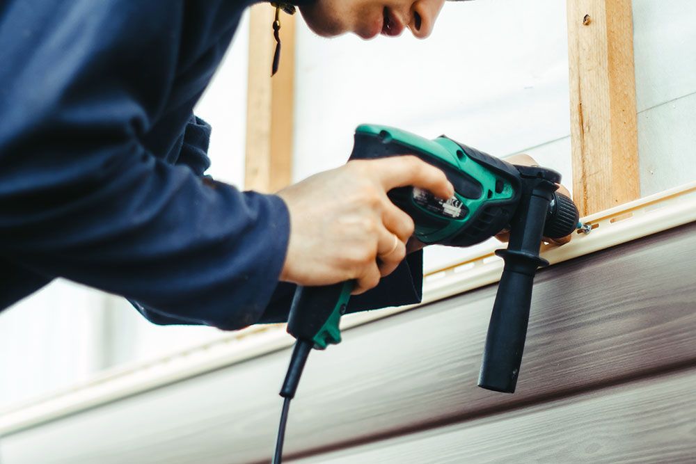 man using nail gun to install house siding
