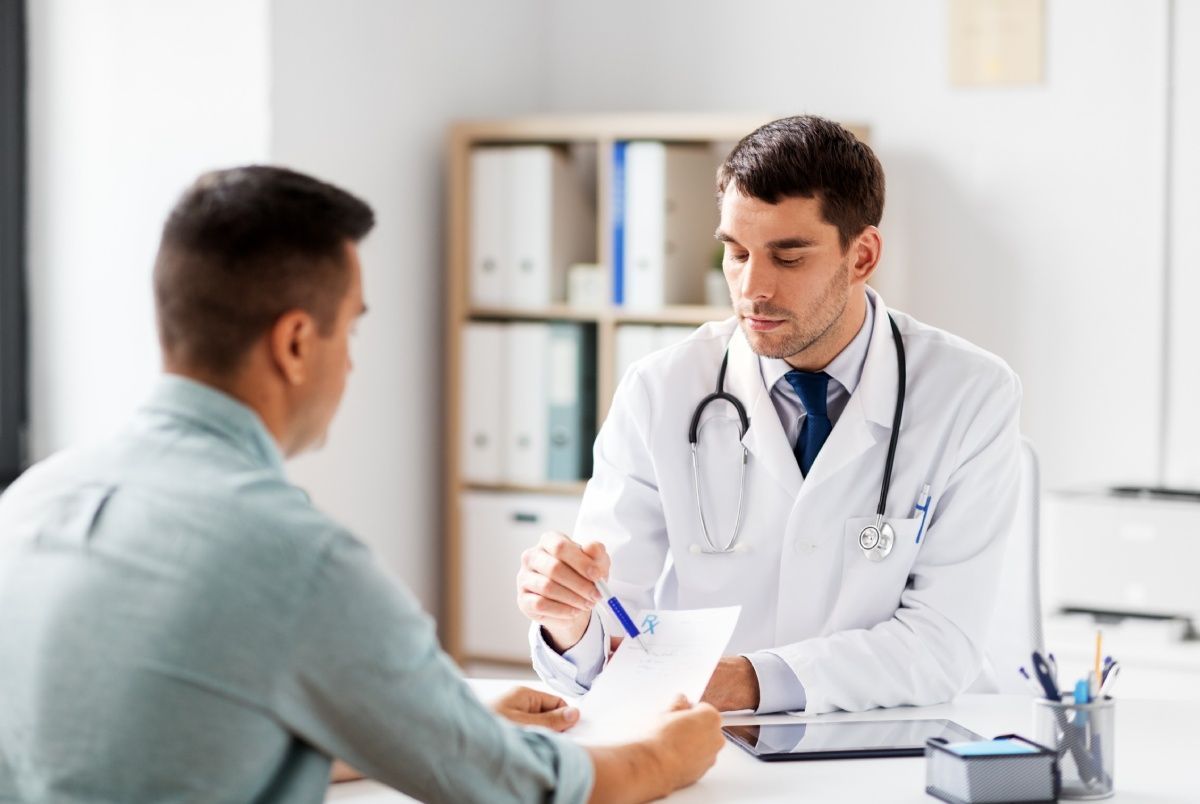 Doctor in white coat reviews paperwork with a patient in an office setting.