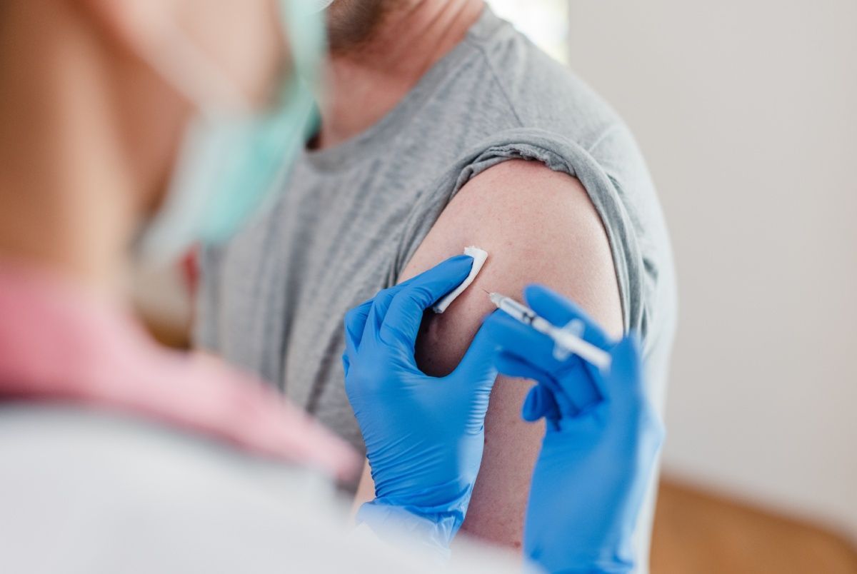 Person getting a shot in the arm; gloved hand holding syringe, cotton swab.
