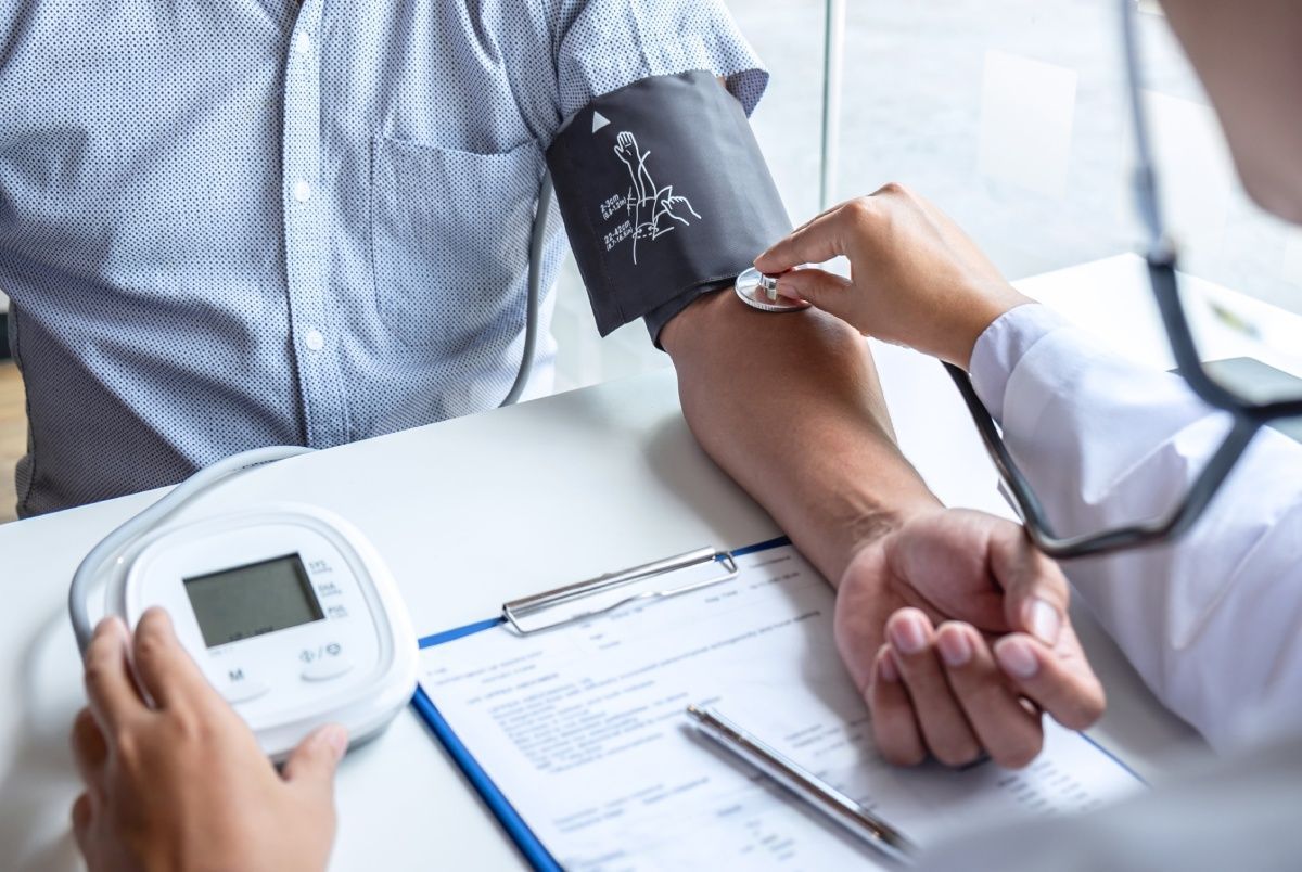 Doctor taking patient's blood pressure with stethoscope and cuff on arm in office setting.