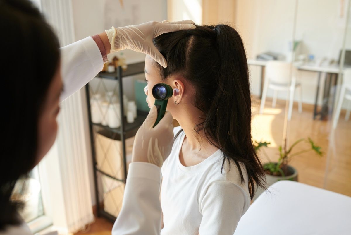 Doctor examining a child's ear with an otoscope in a medical office.