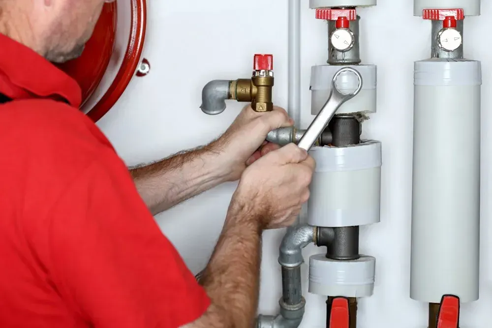 Plumber in Red Shirt Using Wrench on Pipes — Hot Water Systems in Central Coast, NSW