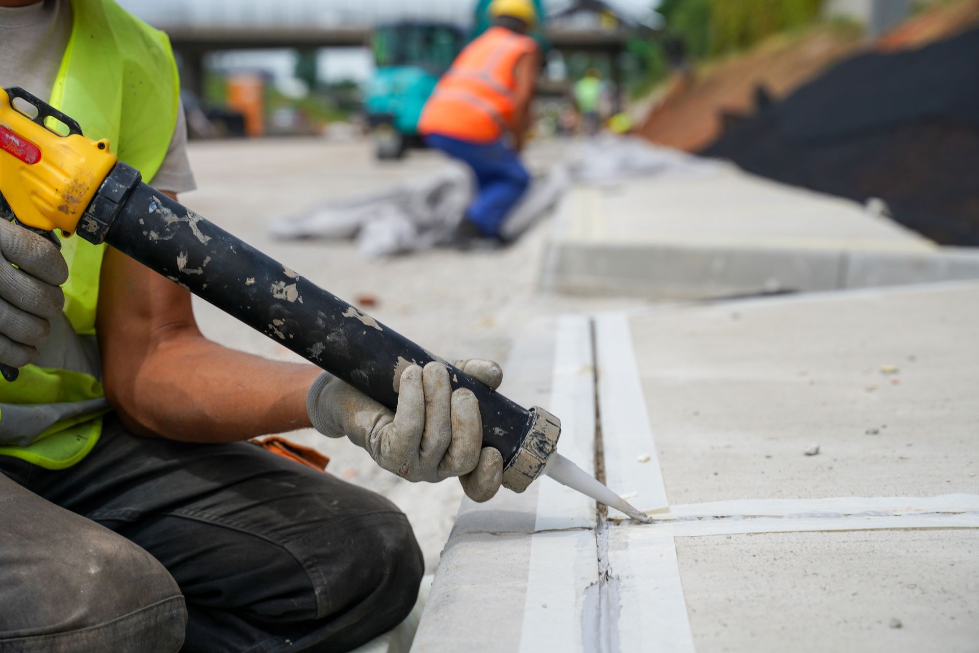 Construction worker applying sealant to a concrete joint using a caulking gun.