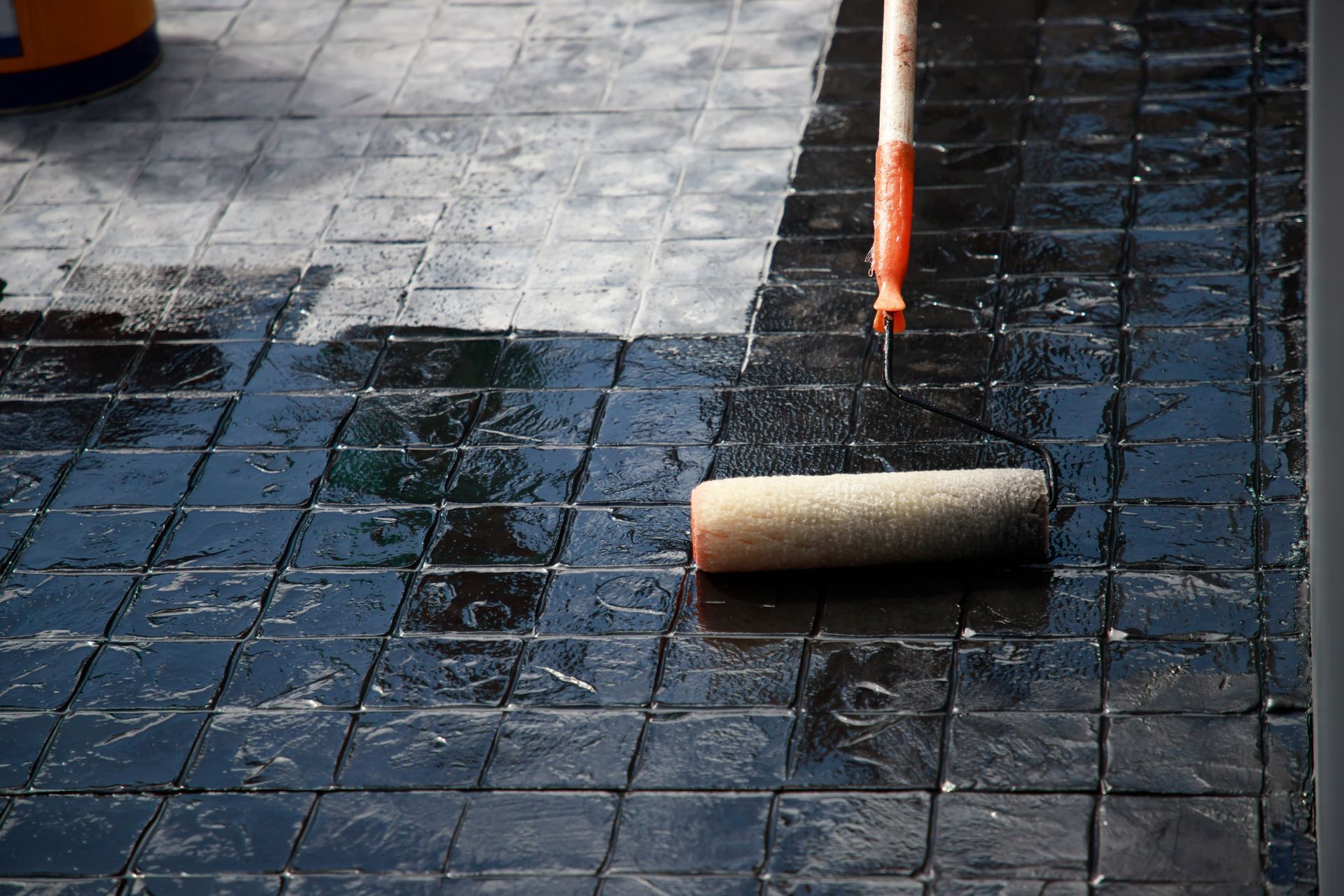 Applying a dark sealant to a textured, brick-patterned concrete surface with a roller.