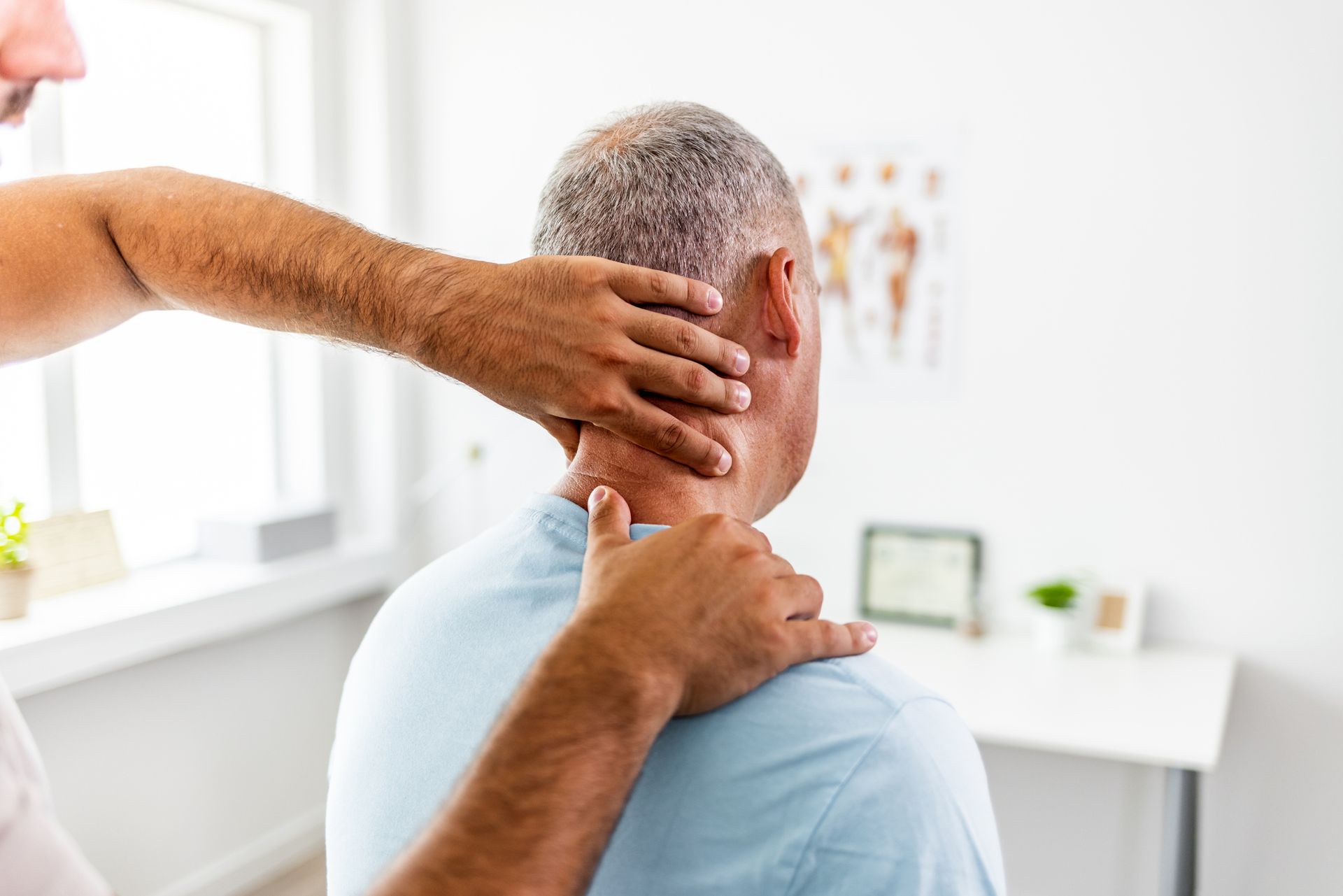 Chiropractor examining a patient's neck in a light-filled office.
