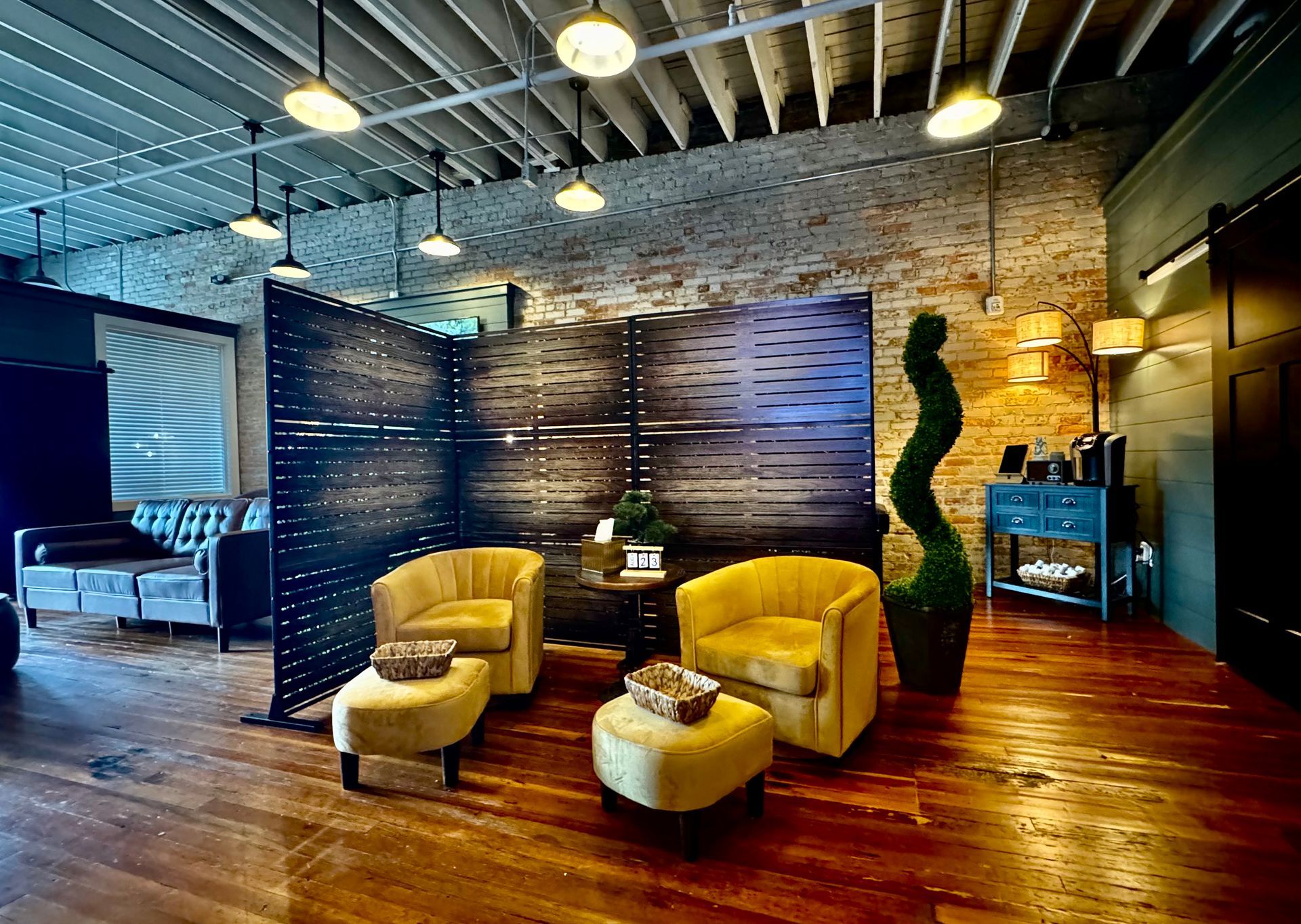 Cozy lounge area with yellow armchairs, ottoman, decorative screen, exposed brick, and wooden floor.