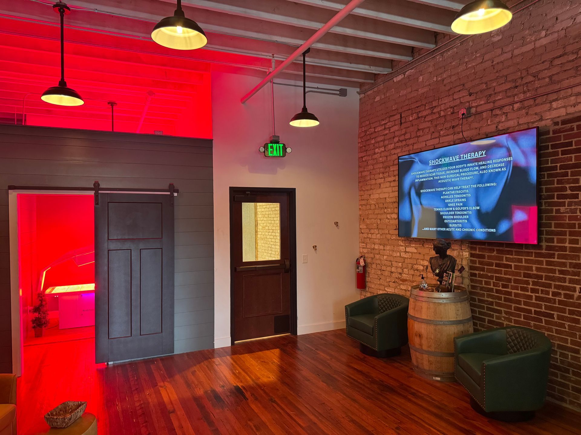Interior with exposed brick, wood floors, dark furniture, a large screen, and red lighting.