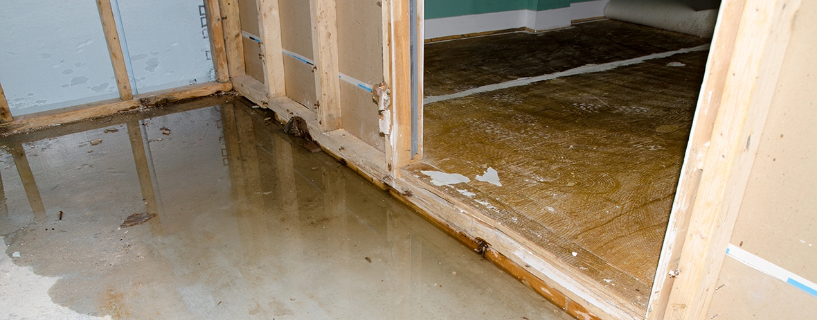 A flooded indoor room with standing water on a concrete floor and damp wooden wall framing.