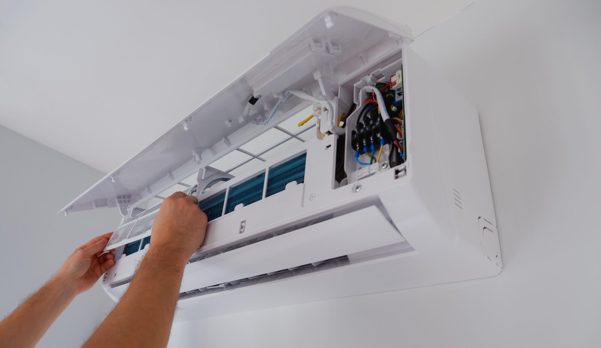 Hands installing an air conditioner filter on a white wall-mounted unit.