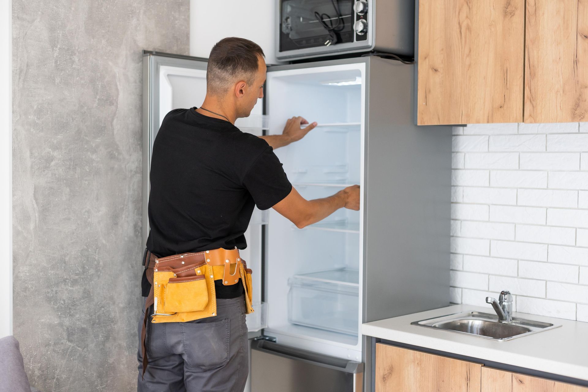 Man in work belt inspects inside of refrigerator in kitchen.