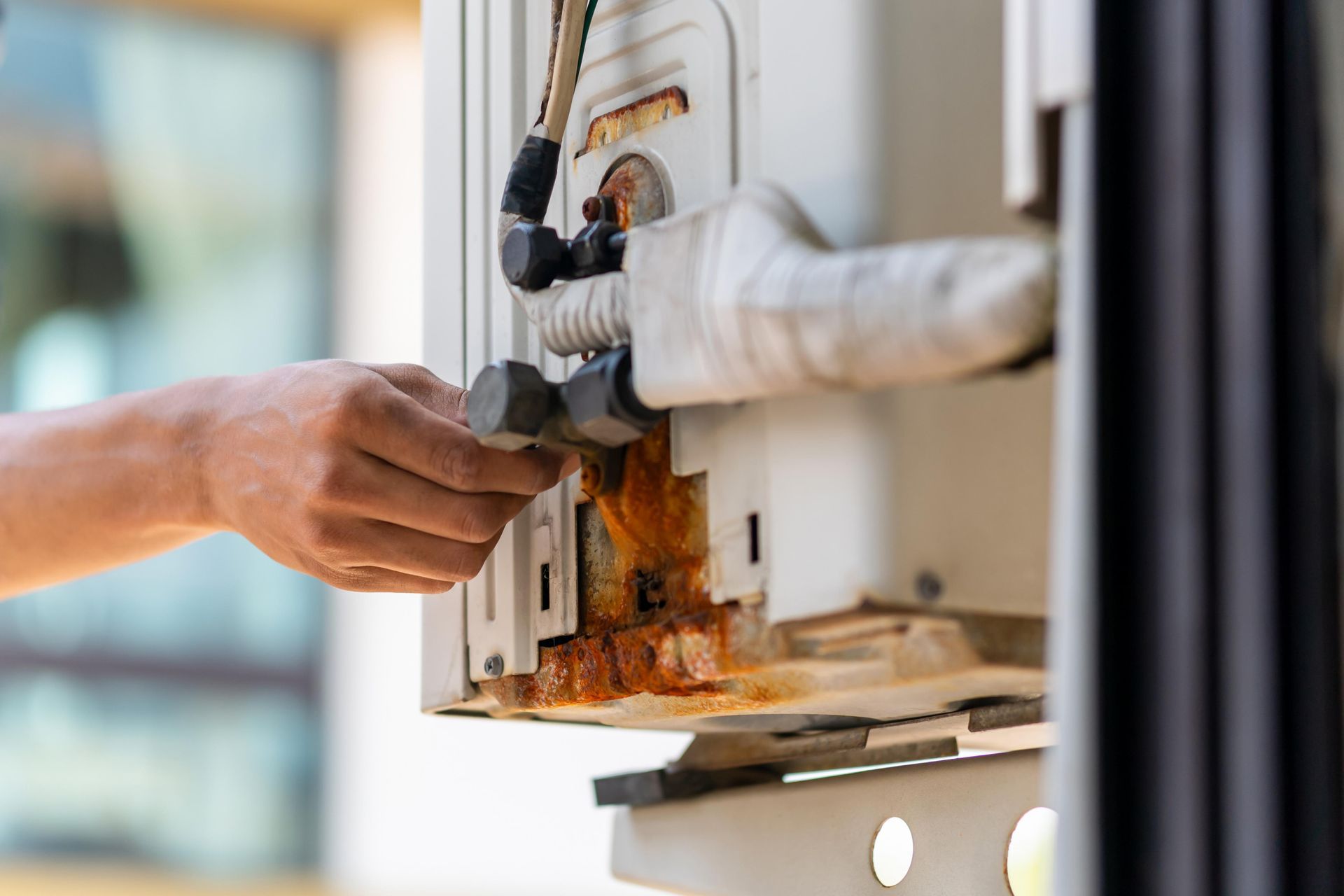 Hand inspecting a rusty white appliance, likely a water heater, outdoors.