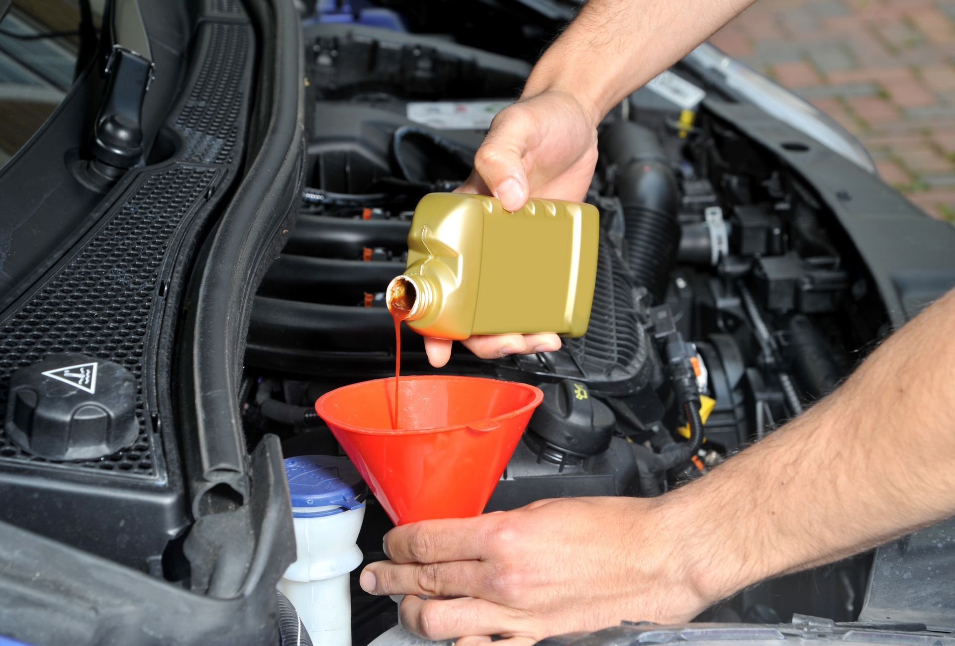 Close-up of a hand pouring radiator fluid to a vehicle with a red funnel.