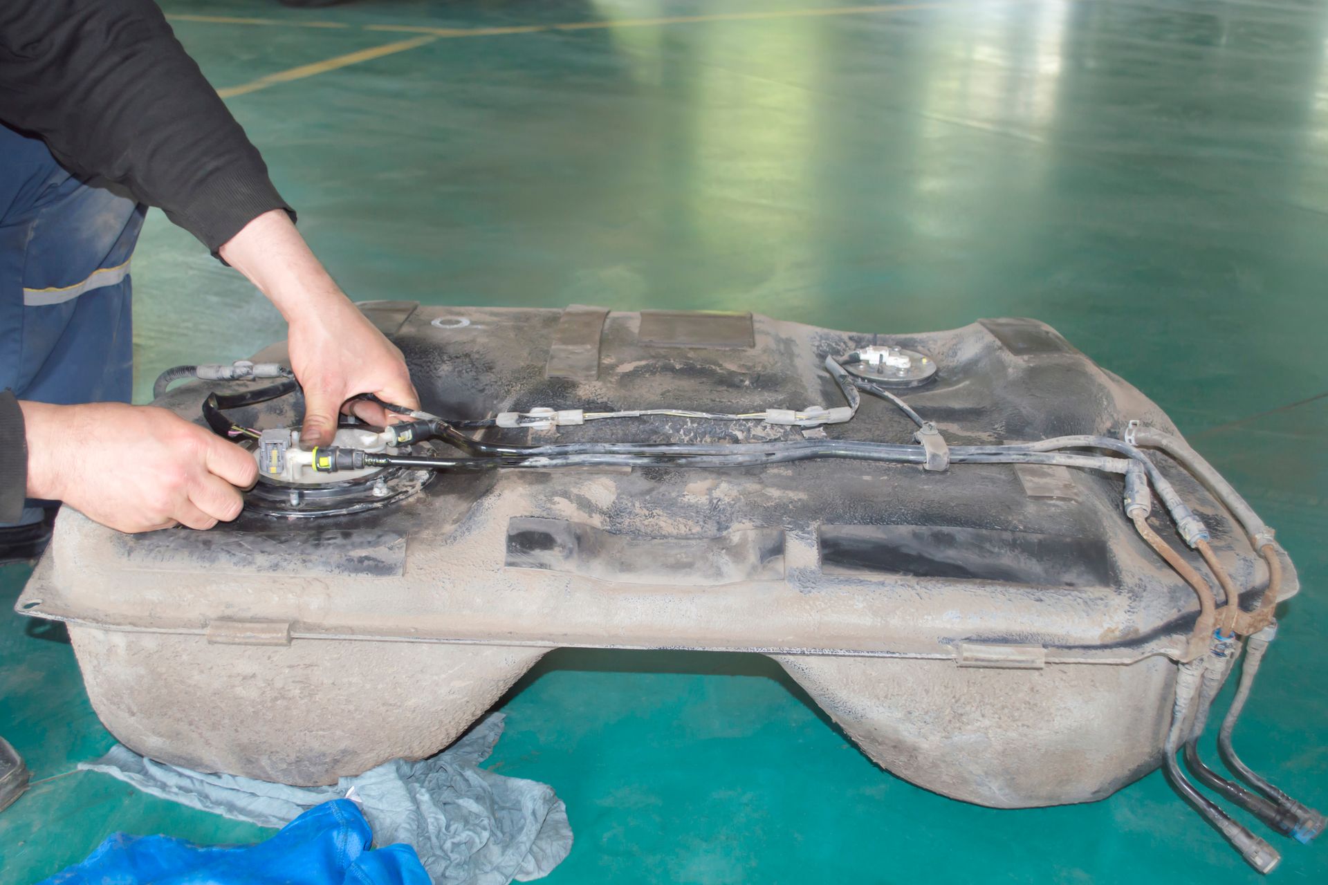A person is working on a fuel tank on a green floor.