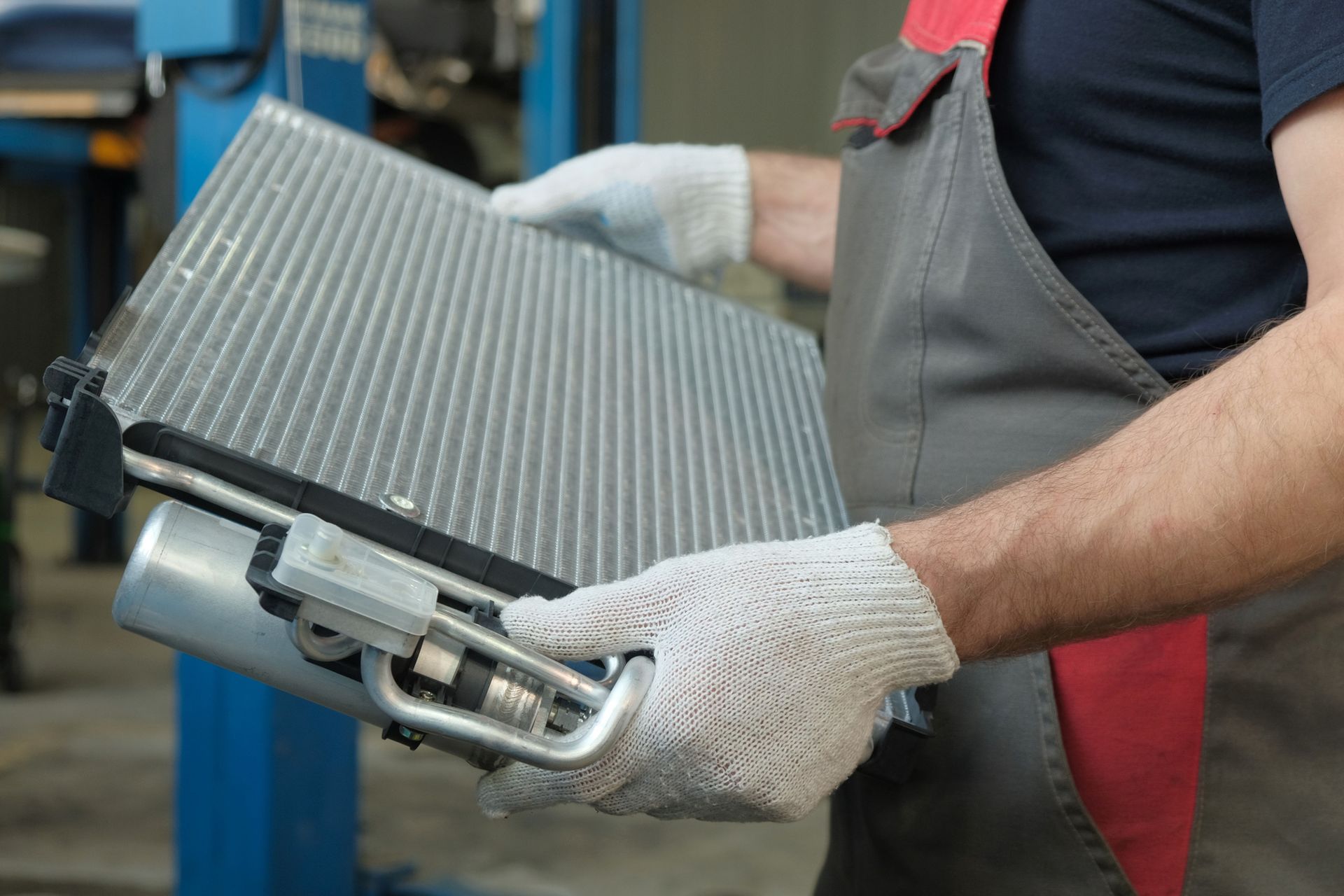 Mechanic holding a car radiator in auto workshop.