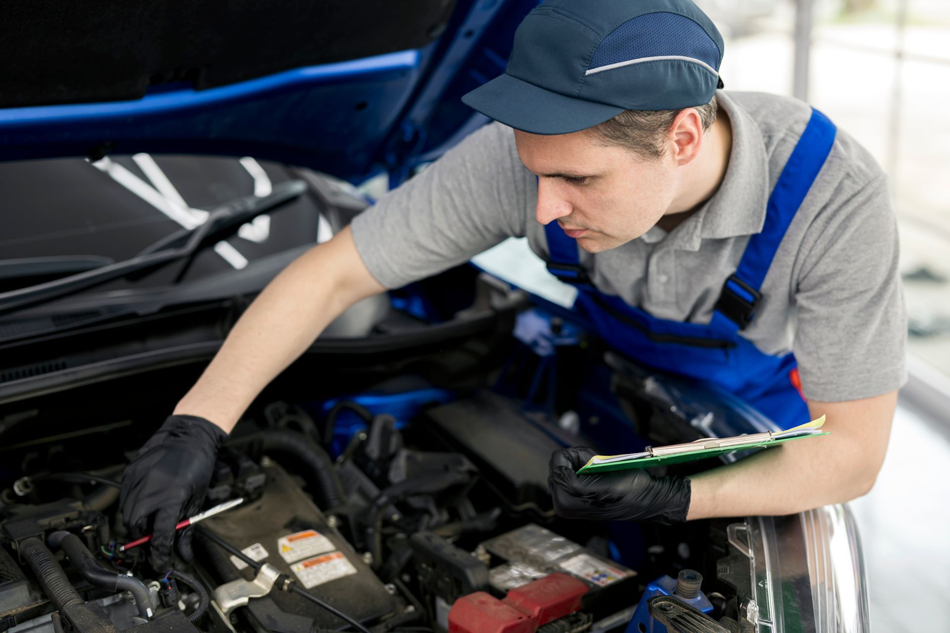 Mechanic in uniform working on car engine with hood open.