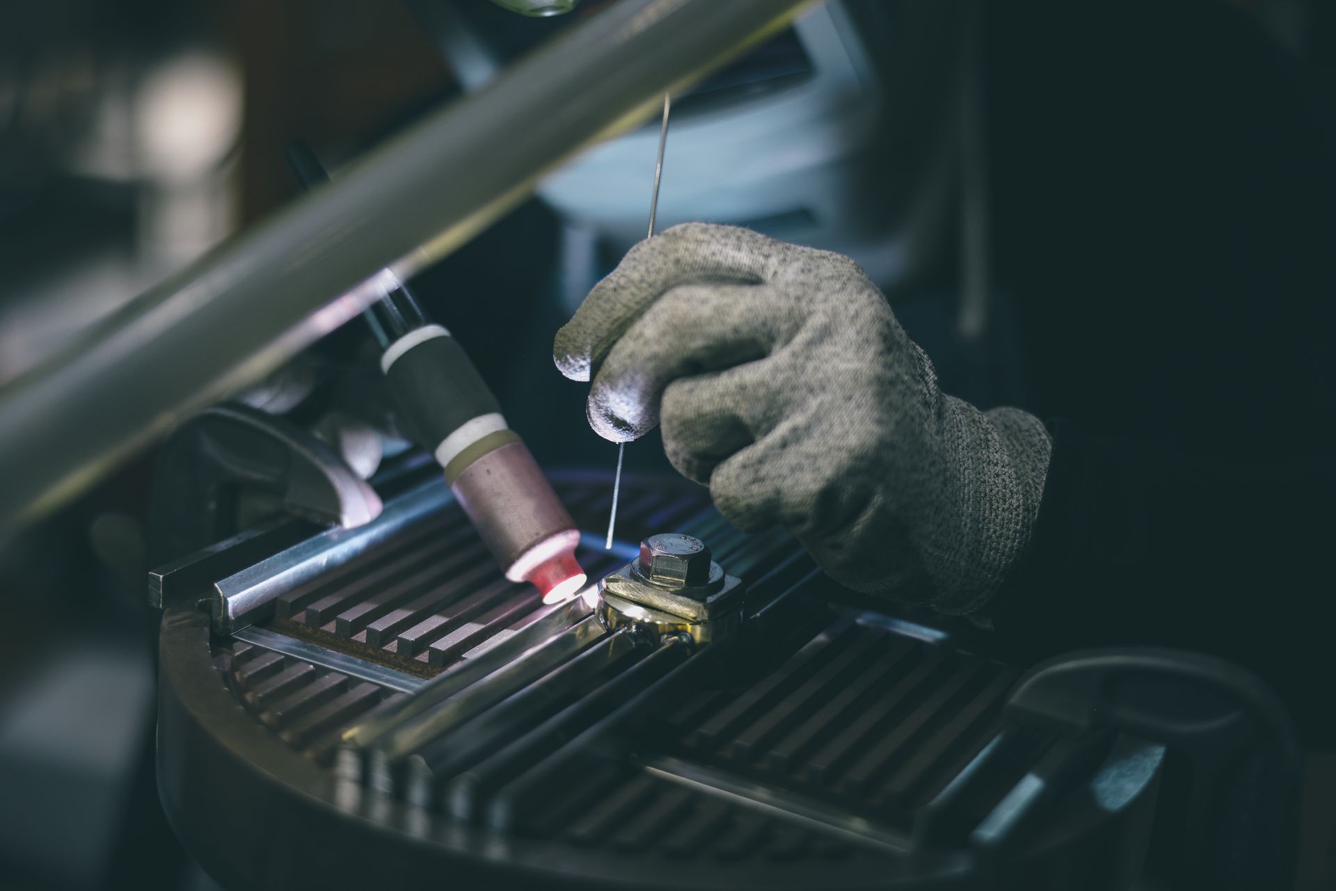 Close-up of welding metal in workshop with protective gloves, sparks, and industrial equipment.