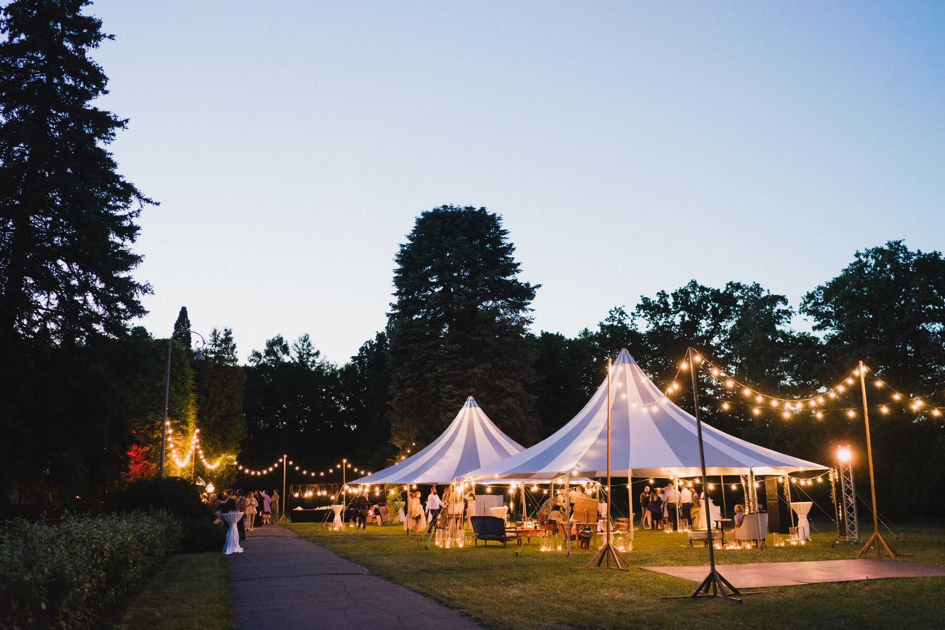 Outdoor evening event with illuminated tents and string lighting.