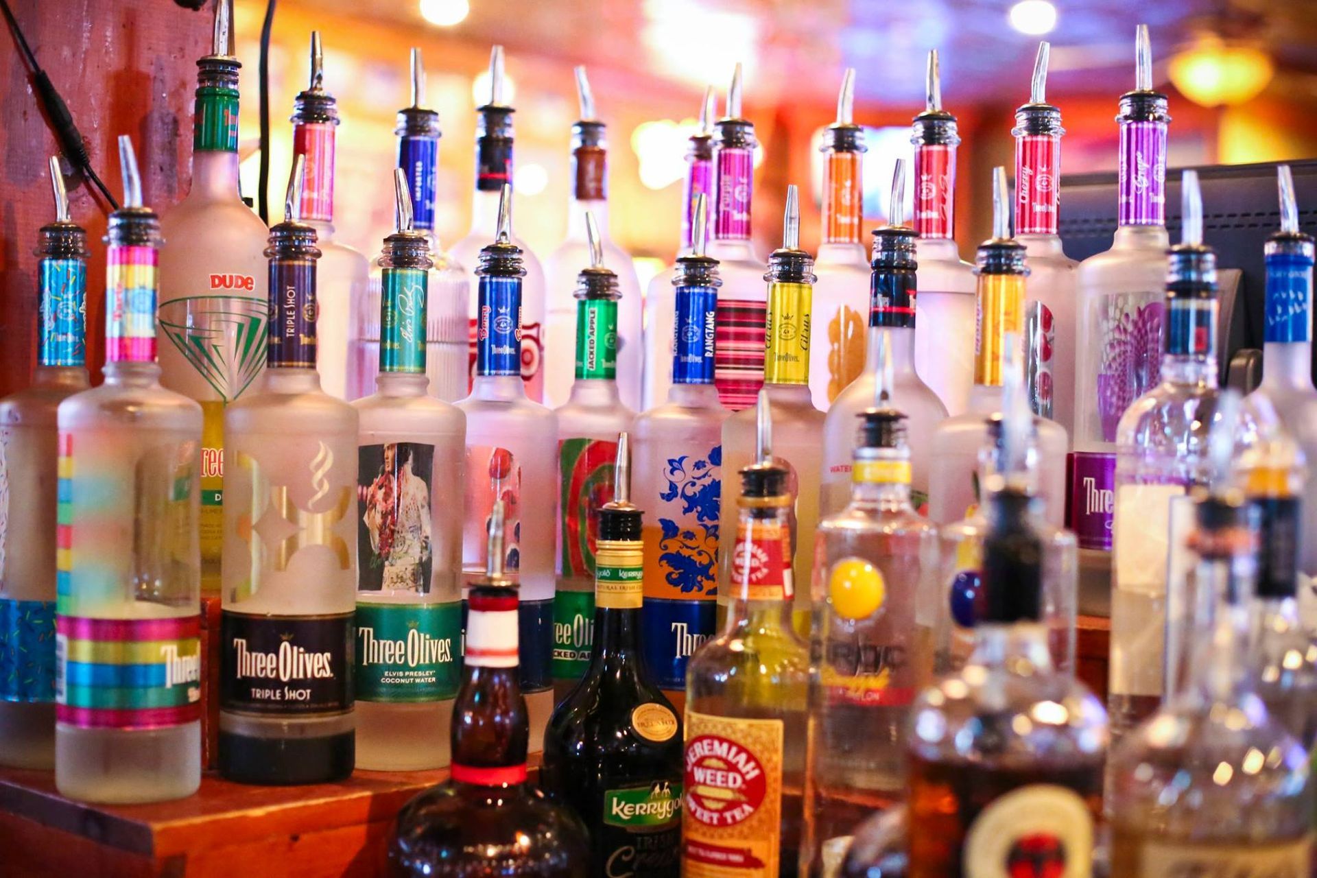 Liquor bottles with colorful pour spouts arranged on a bar, ready for use.