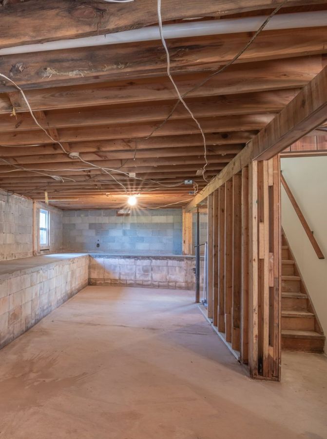 An empty basement with a wooden ceiling and stairs.