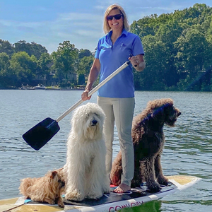 A woman is standing on a paddle board with two dogs