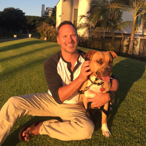 A man is kneeling on the grass holding a dog