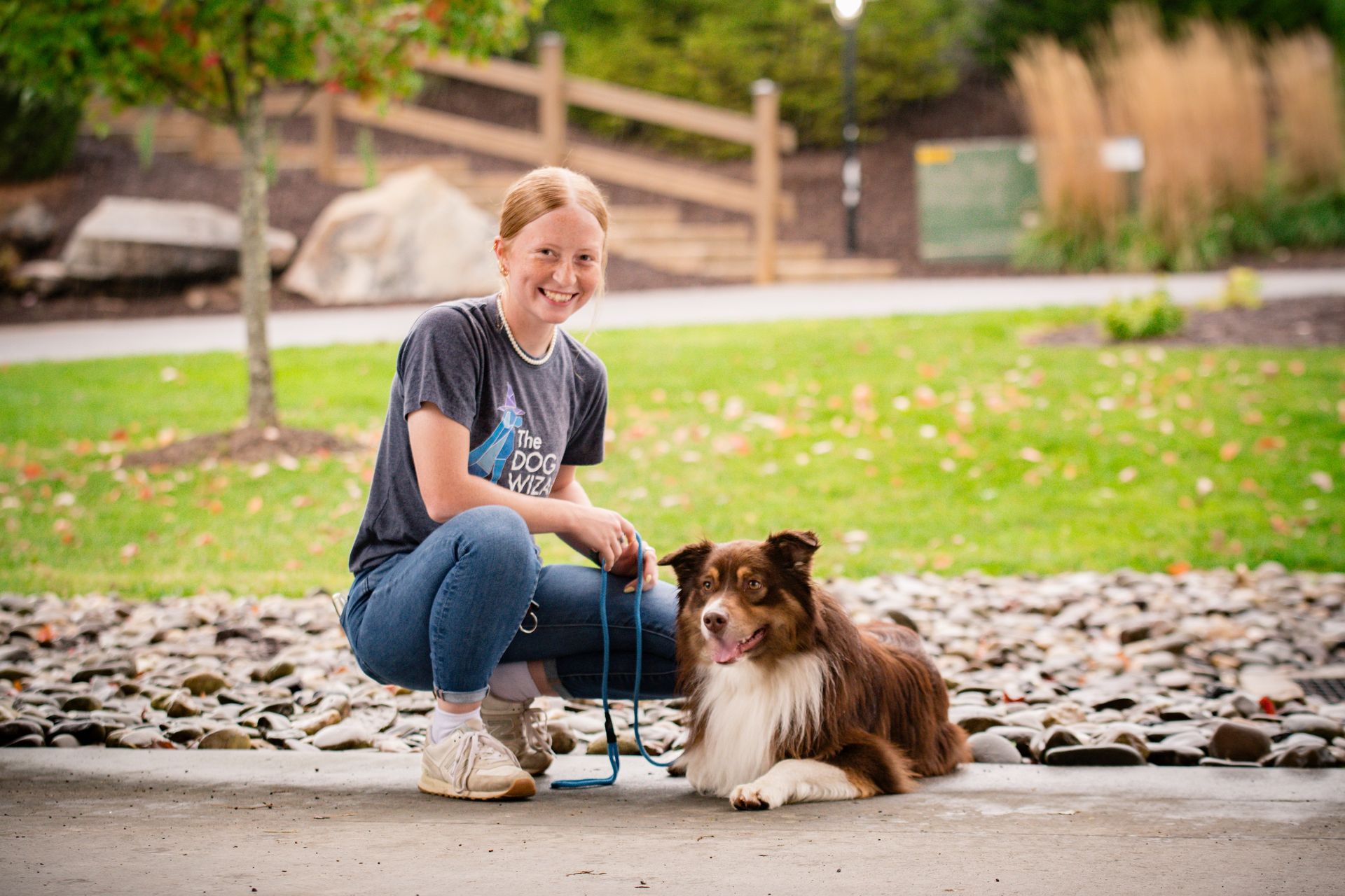 A woman is kneeling down next to a dog on a leash.