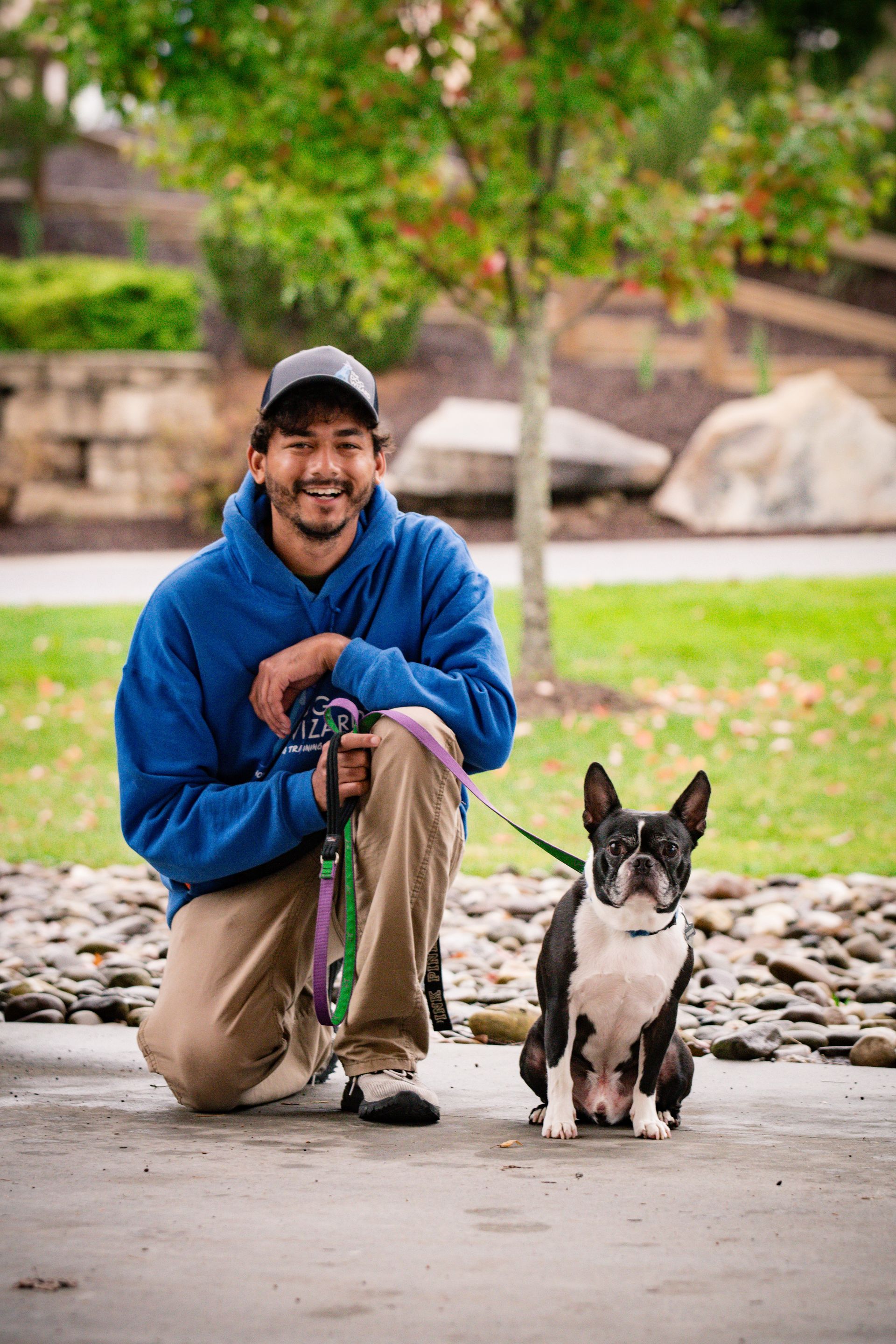 A man is kneeling down next to a small dog on a leash.